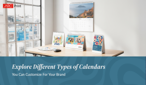 Desk setup with multiple 2026 custom desk calendars and a wall calendar displaying scenic photography, placed near a large window. Text below reads ‘Explore Different Types of Calendars You Can Customize For Your Brand.